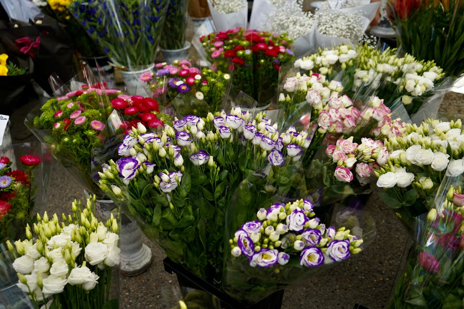A collection of fresh floral bouquets displayed on a dark surface, featuring a variety of flowers including purple and white irises, pink and white roses, white lisianthus, and red and pink chrysanthe