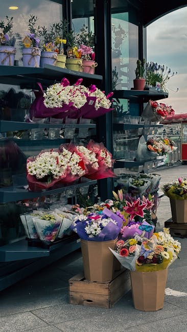 A display of various flower arrangements and bouquets at Kilburn Florist, showcasing a mix of fresh flowers including white chrysanthemums, pink lilies, purple asters, and mixed seasonal blooms, wrapp